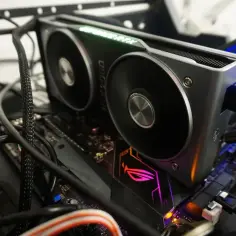 Karta graficzna RTX 2060 z zielonym podświetleniem "GeForce RTX" i dwoma wentylatorami, podłączona do płyty głównej z podświetlanym logo ROG. Dużo kabli, w tym zasilających, otacza komponenty. VRAM tej karty zapewnia płynność w grach.